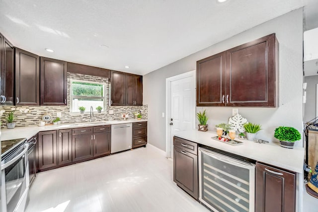 kitchen featuring appliances with stainless steel finishes, sink, backsplash, beverage cooler, and dark brown cabinetry