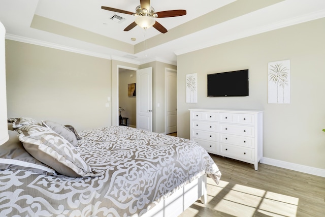 bedroom with ceiling fan, ornamental molding, a raised ceiling, and light hardwood / wood-style flooring