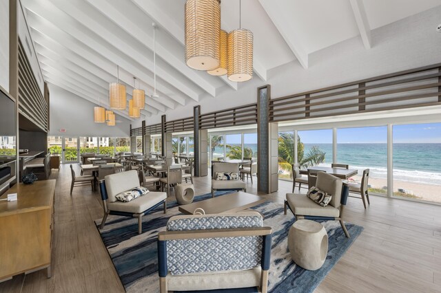 living room with a water view, a view of the beach, hardwood / wood-style flooring, a towering ceiling, and beamed ceiling