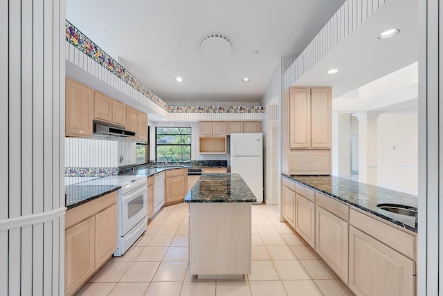 kitchen with white appliances, light tile patterned floors, dark stone counters, a kitchen island, and light brown cabinetry