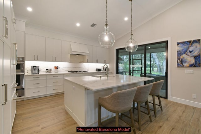 kitchen with lofted ceiling, sink, white cabinetry, custom range hood, and a kitchen island with sink