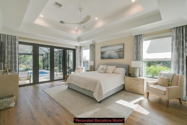 bedroom featuring multiple windows, hardwood / wood-style flooring, a tray ceiling, and access to exterior