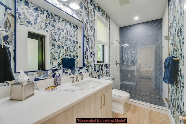 bathroom with toilet, vanity, a tile shower, and wood-type flooring