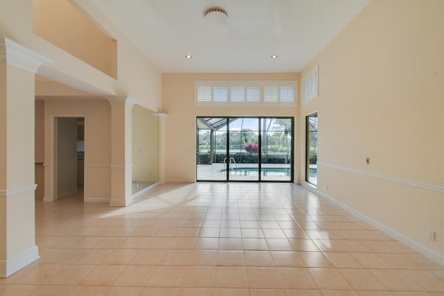 unfurnished room with light tile patterned floors, ornate columns, and a towering ceiling