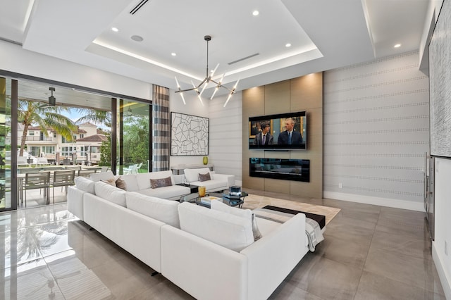 living room with a raised ceiling, a tile fireplace, and an inviting chandelier