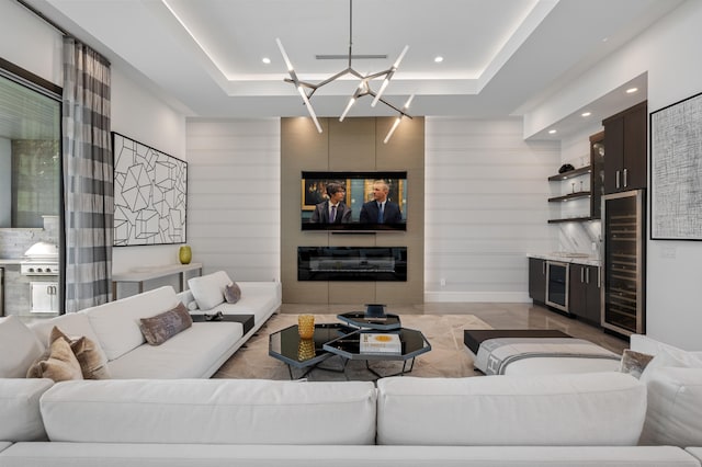 living room with a tray ceiling, wine cooler, a large fireplace, and a notable chandelier