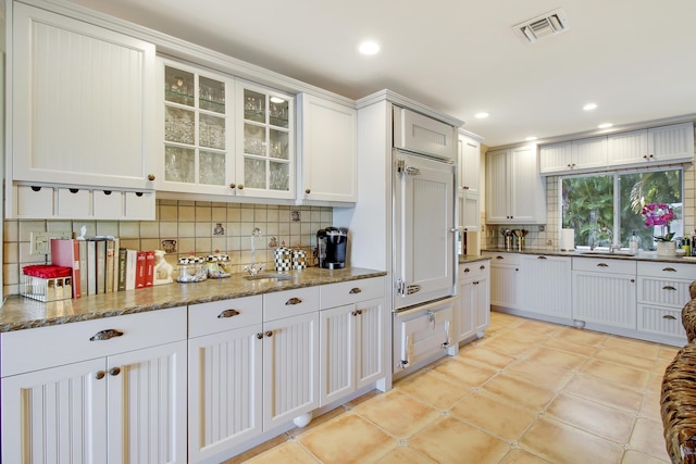 kitchen featuring sink, backsplash, white cabinets, and dark stone countertops