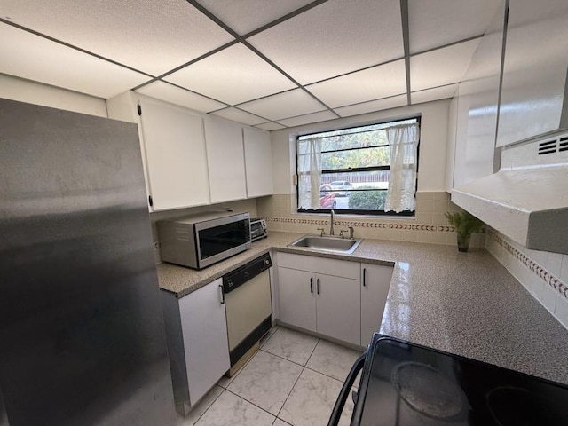 kitchen featuring stainless steel appliances, backsplash, white cabinets, a sink, and a drop ceiling