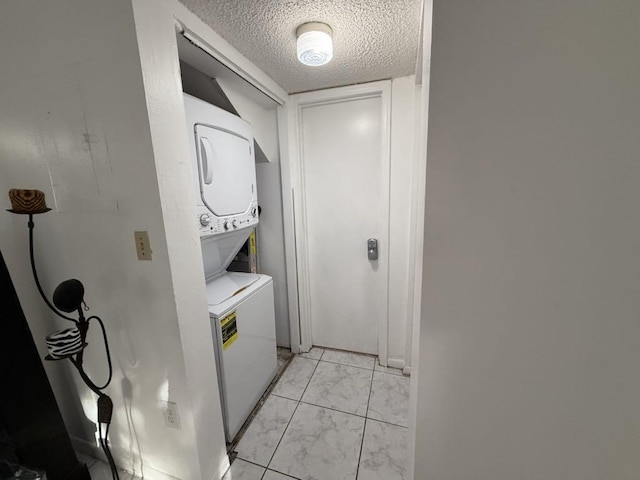 washroom featuring stacked washer and dryer, laundry area, marble finish floor, and a textured ceiling