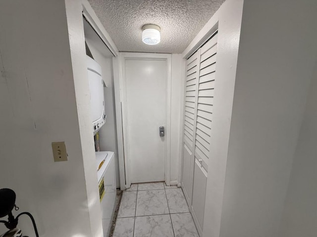 hall with marble finish floor, a textured ceiling, and stacked washer / drying machine