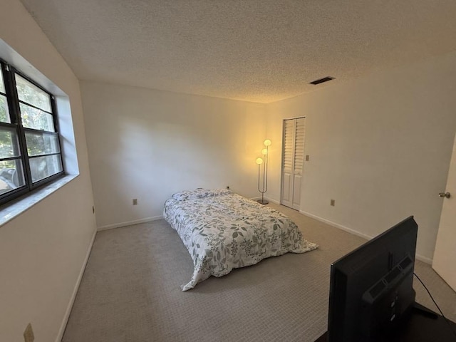 carpeted bedroom featuring a textured ceiling, visible vents, and baseboards