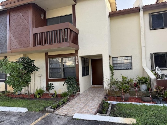 doorway to property featuring uncovered parking, a balcony, and stucco siding