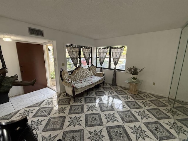 living area with a textured ceiling, light tile patterned floors, visible vents, and baseboards