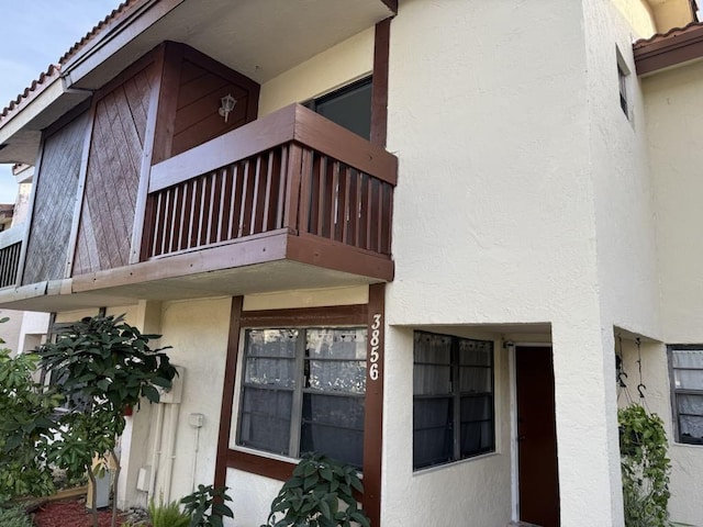 view of exterior entry with a tiled roof, a balcony, and stucco siding