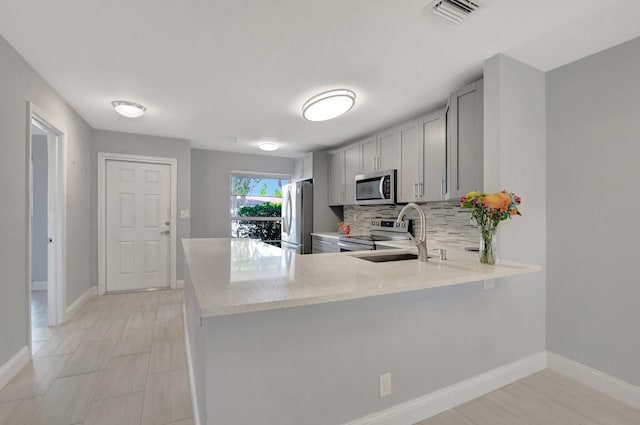 kitchen featuring sink, gray cabinets, appliances with stainless steel finishes, tasteful backsplash, and kitchen peninsula