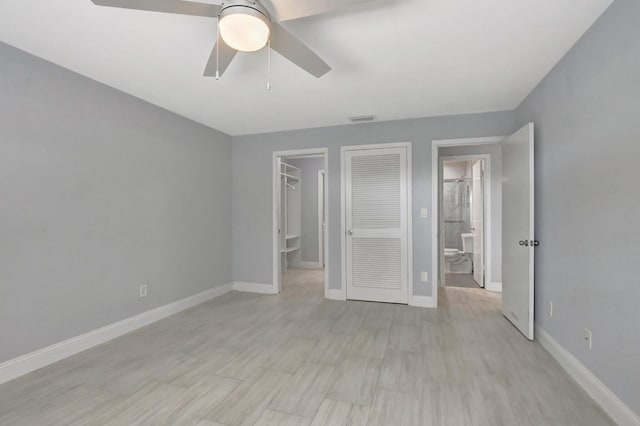 unfurnished bedroom featuring a closet, ceiling fan, ensuite bathroom, and a spacious closet