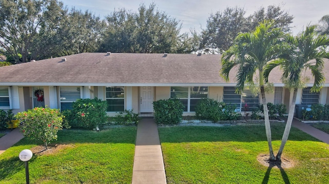 view of front facade featuring roof with shingles, a front lawn, and stucco siding