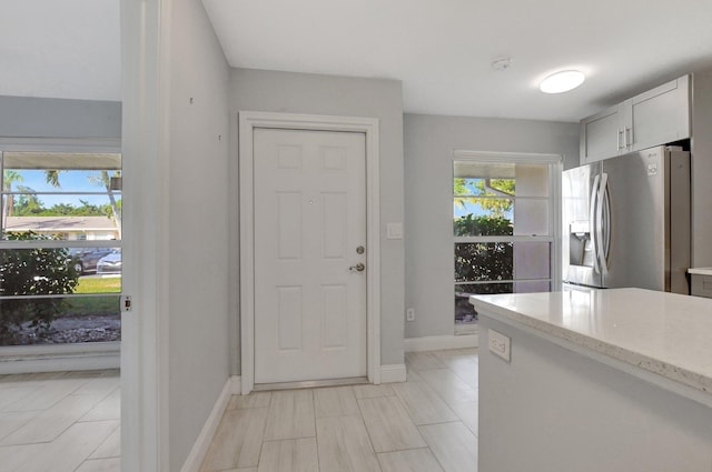 kitchen featuring baseboards, stainless steel refrigerator with ice dispenser, and light stone countertops