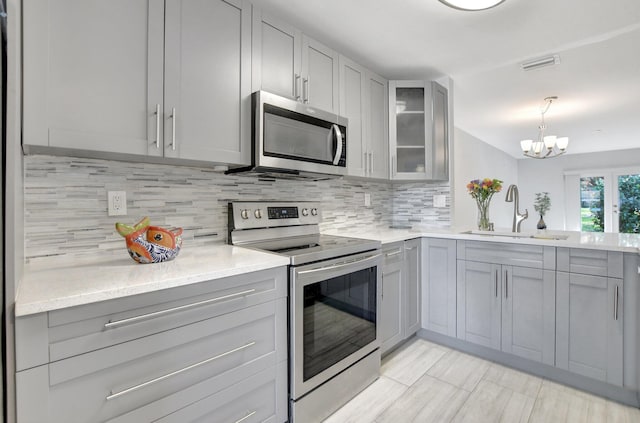 kitchen featuring sink, gray cabinets, decorative light fixtures, stainless steel appliances, and a chandelier