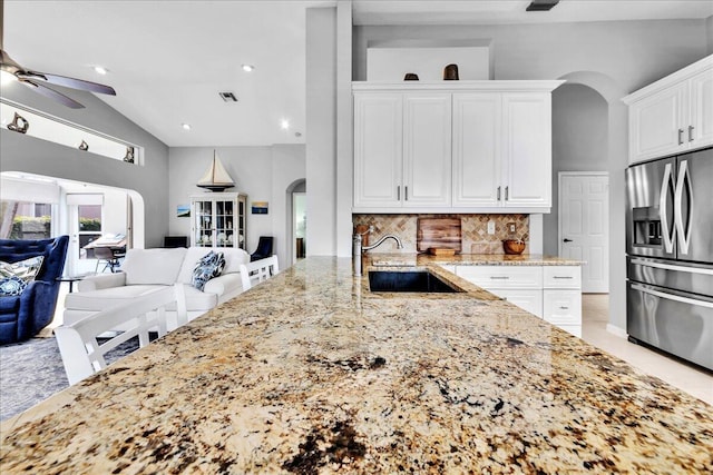 kitchen featuring backsplash, sink, stainless steel fridge with ice dispenser, light stone counters, and white cabinetry