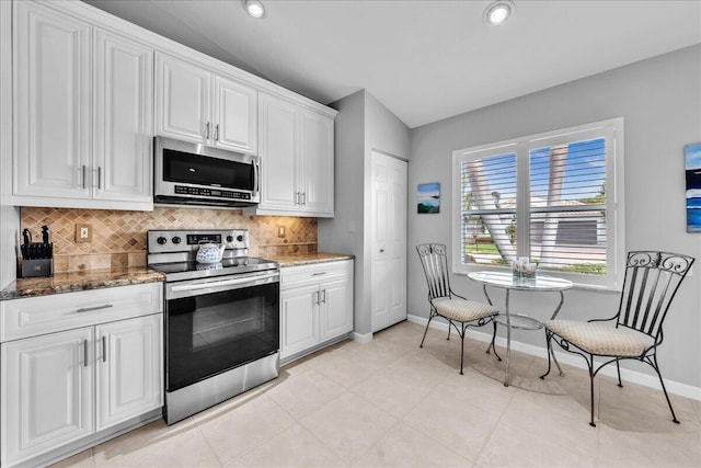 kitchen with stainless steel appliances, vaulted ceiling, white cabinetry, and dark stone counters