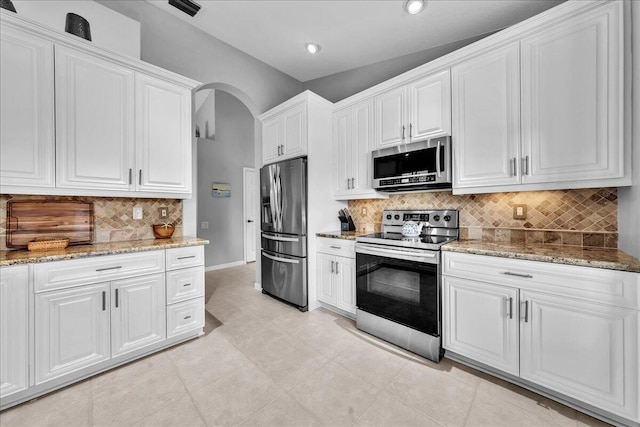 kitchen featuring light stone countertops, lofted ceiling, decorative backsplash, white cabinets, and appliances with stainless steel finishes