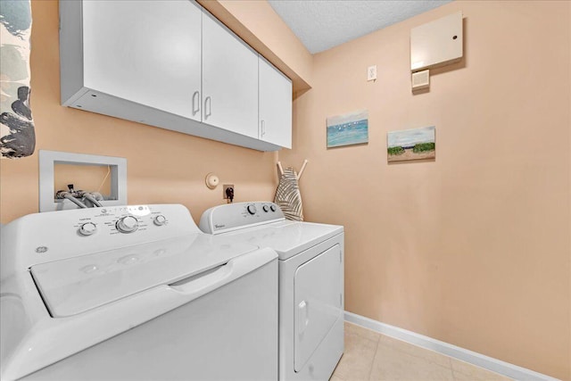 laundry area featuring washer and clothes dryer, light tile patterned floors, cabinets, and a textured ceiling