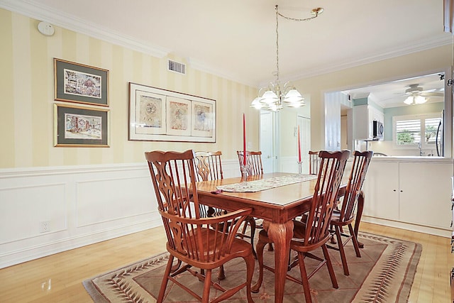 dining area featuring ceiling fan with notable chandelier, light wood-type flooring, and crown molding