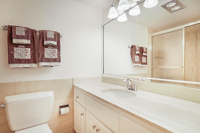 bathroom with vanity, toilet, a shower with shower door, and tile walls