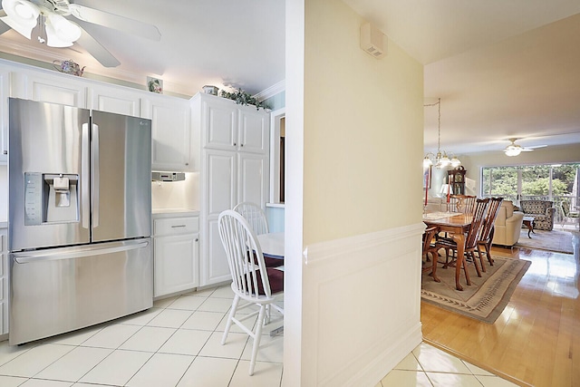 kitchen with stainless steel fridge, white cabinets, light tile patterned flooring, and ceiling fan with notable chandelier