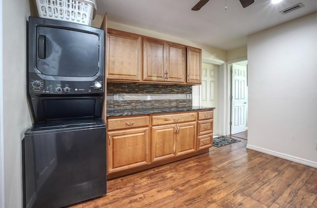 kitchen with dark stone counters, ceiling fan, decorative backsplash, stacked washer / drying machine, and dark hardwood / wood-style flooring