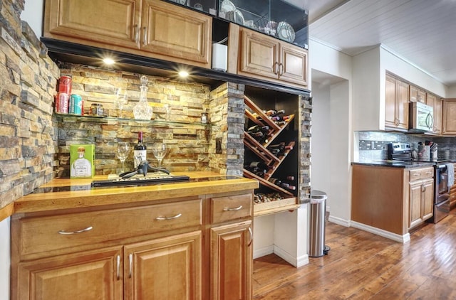 bar with decorative backsplash, appliances with stainless steel finishes, wooden counters, and wood-type flooring