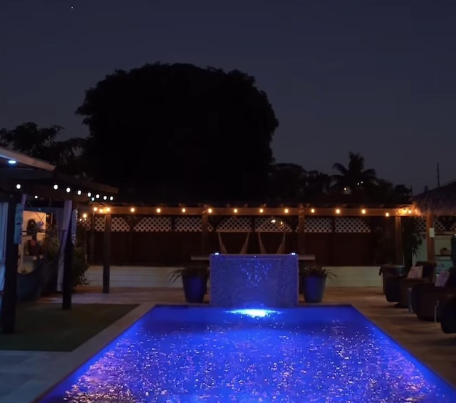 pool at twilight with pool water feature and a patio