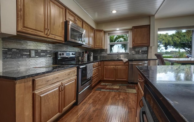 kitchen with backsplash, stainless steel appliances, dark wood-type flooring, sink, and dark stone countertops