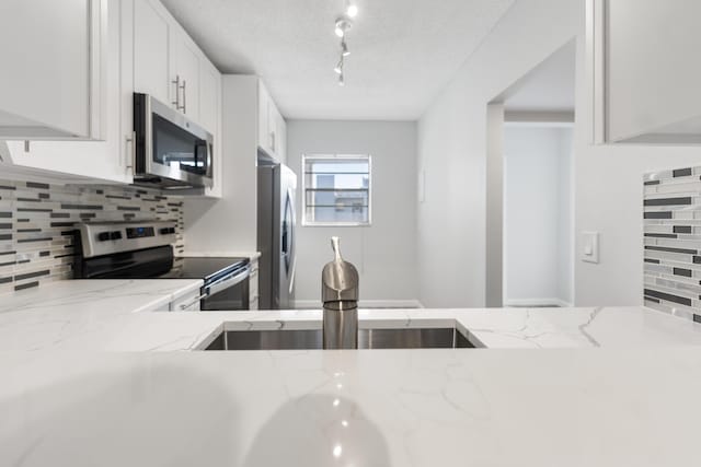 kitchen with light stone countertops, rail lighting, a textured ceiling, white cabinets, and appliances with stainless steel finishes