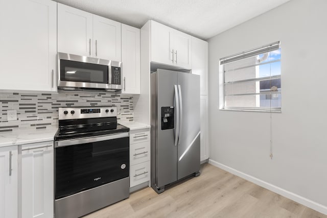 kitchen with white cabinets, a textured ceiling, appliances with stainless steel finishes, light hardwood / wood-style floors, and light stone counters