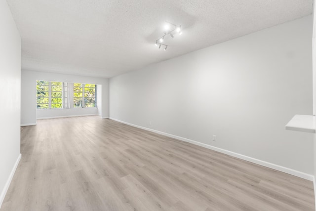 spare room featuring light wood-type flooring, a textured ceiling, and track lighting