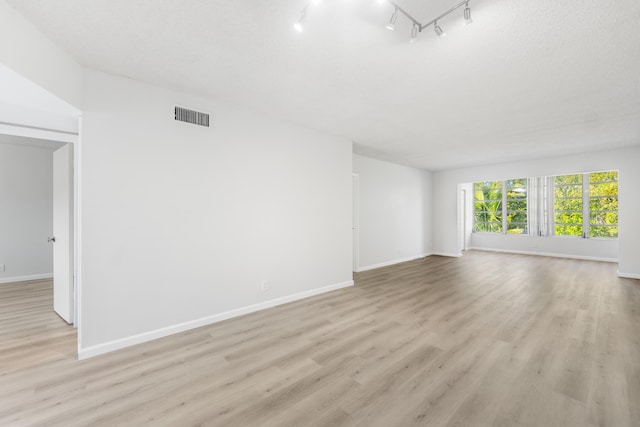 spare room featuring light wood-type flooring, a textured ceiling, and track lighting