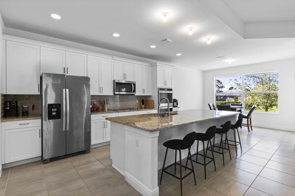 kitchen with white cabinets, stainless steel appliances, a kitchen island with sink, and sink