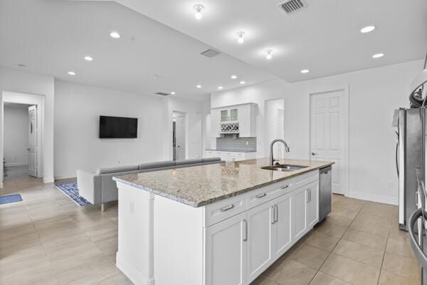 kitchen with white cabinets, an island with sink, light stone countertops, and sink