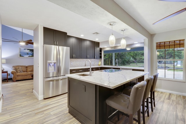 kitchen featuring pendant lighting, sink, stainless steel fridge, light stone counters, and black electric cooktop