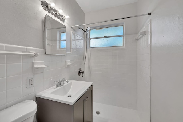 bathroom featuring vanity, toilet, tiled shower, and tile walls