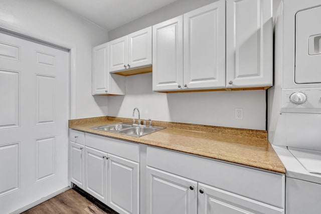 kitchen with white cabinets, sink, stacked washer and dryer, and hardwood / wood-style flooring