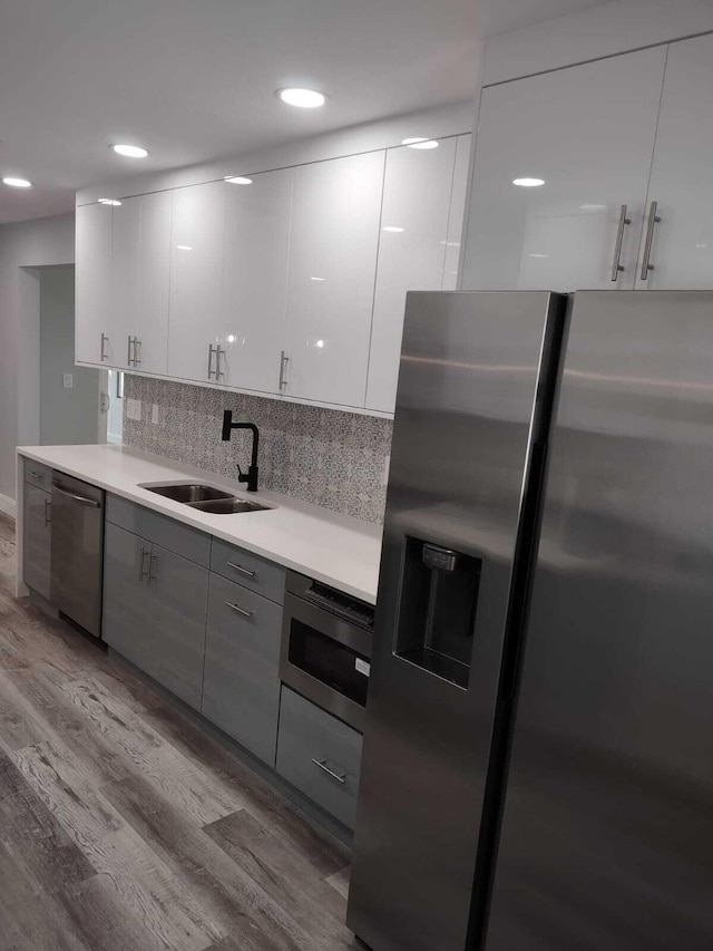 kitchen with white cabinets, sink, light hardwood / wood-style flooring, decorative backsplash, and stainless steel appliances