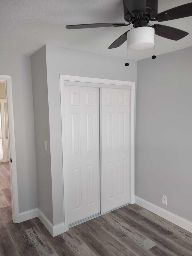 unfurnished bedroom with ceiling fan, a closet, and dark wood-type flooring