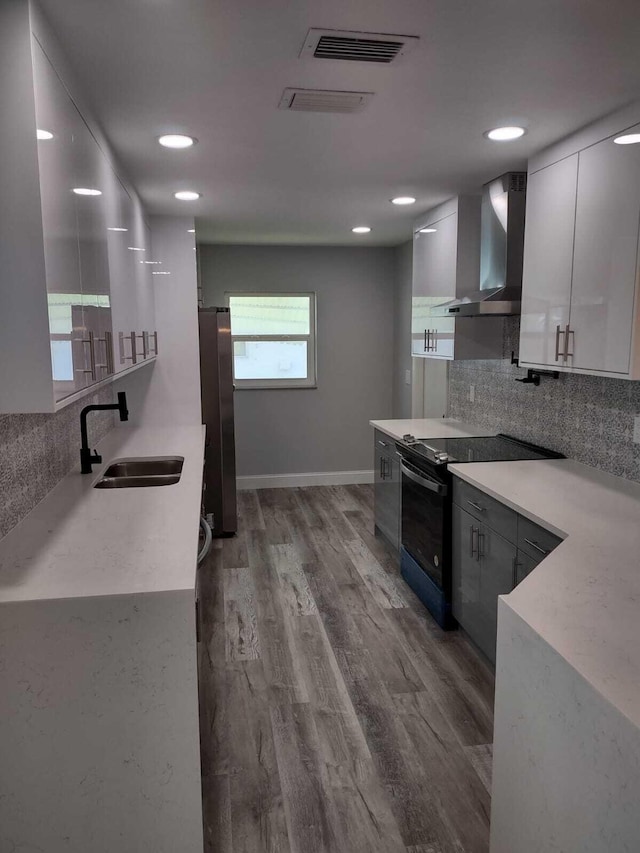 kitchen featuring electric range, sink, wall chimney exhaust hood, tasteful backsplash, and hardwood / wood-style floors