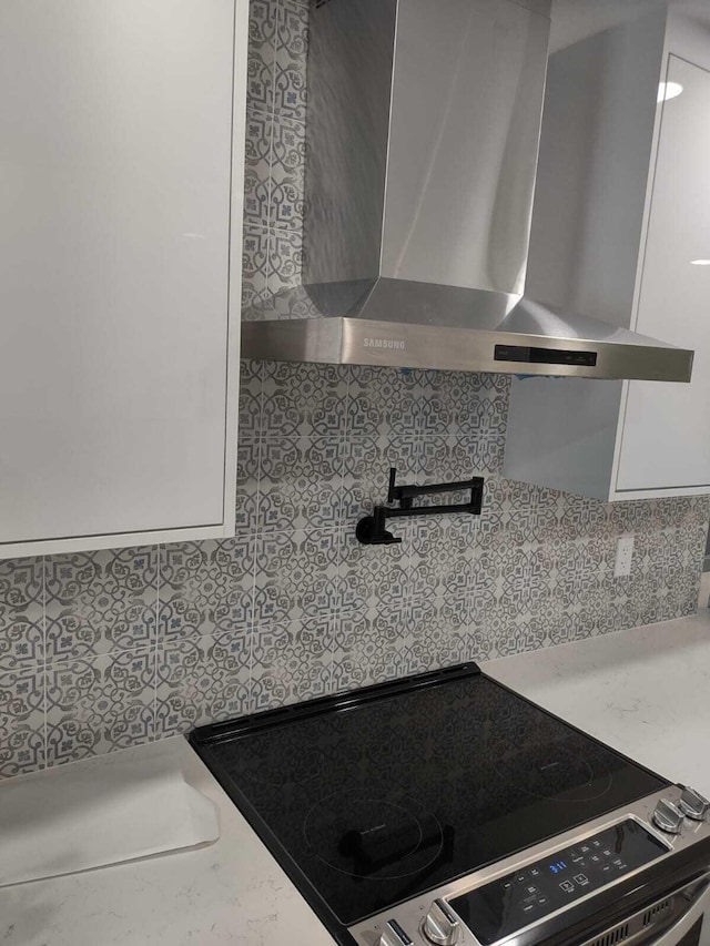 kitchen featuring white cabinetry, stove, and wall chimney range hood