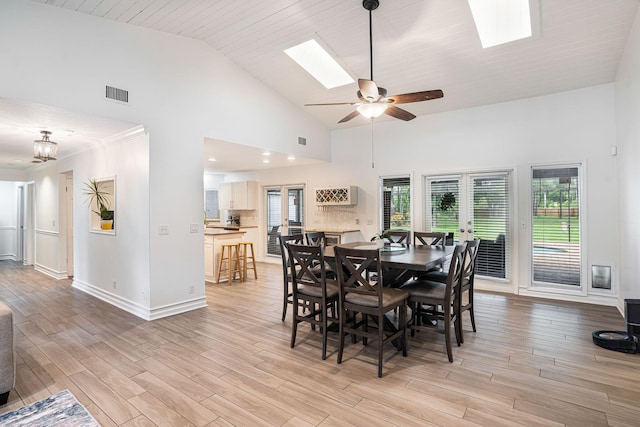 dining room featuring a skylight, ceiling fan, high vaulted ceiling, and light wood-type flooring