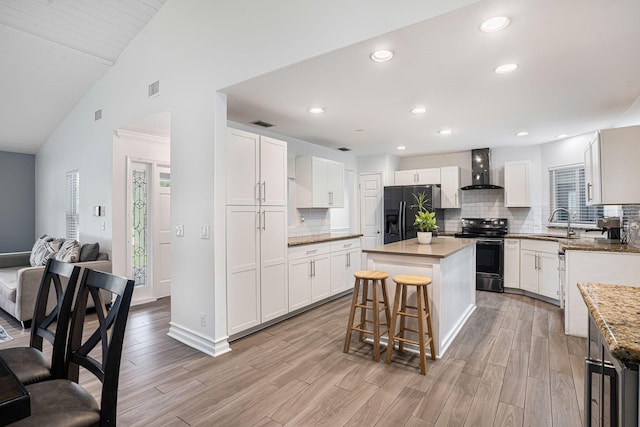 kitchen featuring wall chimney exhaust hood, black fridge with ice dispenser, vaulted ceiling, electric stove, and a kitchen island