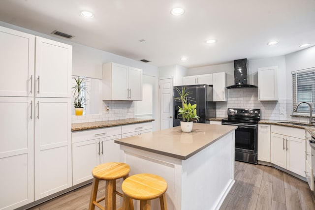 kitchen with refrigerator, sink, wall chimney range hood, range with electric stovetop, and a breakfast bar area